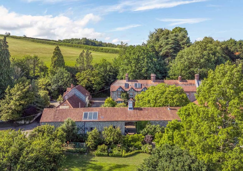 The house and its long barn ranges from above, with pasture rising behind.