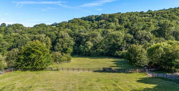 Fenced pasture falling away towards a wooded valley side.