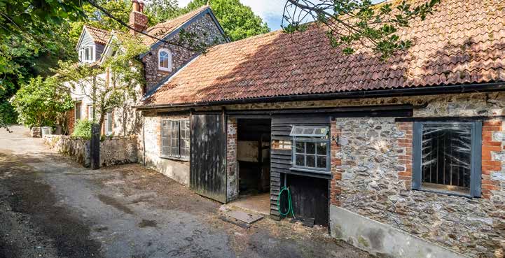 The West Barn Range in stone and cob with open cart bays, the cottage beyond.