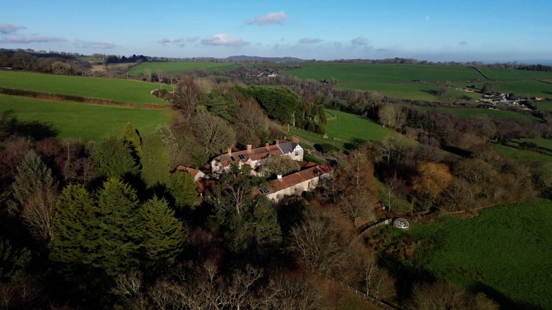 Aerial view of the house among bare winter trees, with green fields all around.