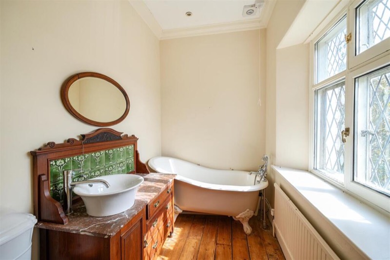 A bathroom with a roll-top bath on claw feet and a marble-topped washstand.