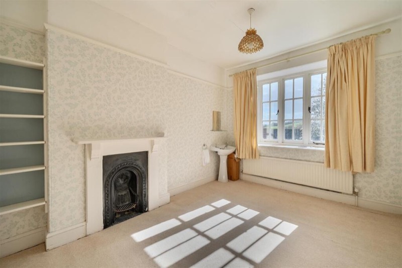A carpeted bedroom with patterned wallpaper and a cast-iron fireplace.