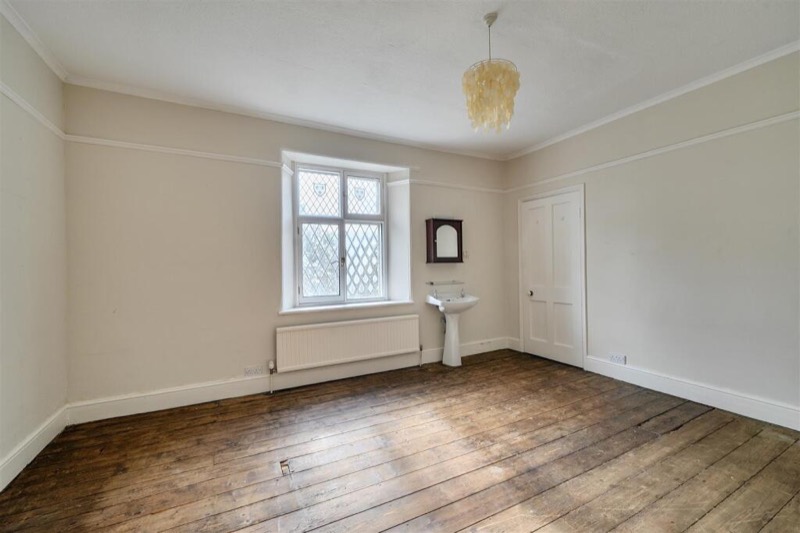 A bedroom with a leaded window, corner basin and bare pine floorboards.