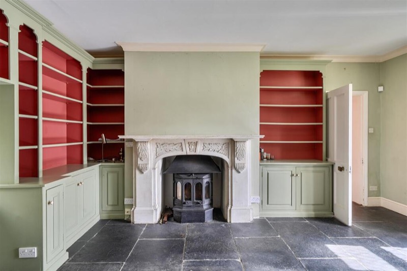 The library with red-backed fitted shelving and a woodburner.