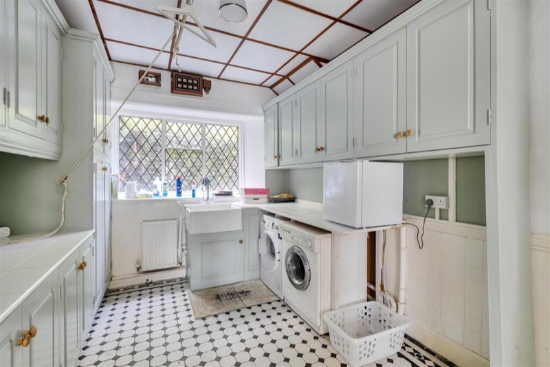 The utility room with a Belfast sink, fitted cupboards and a patterned tiled floor.
