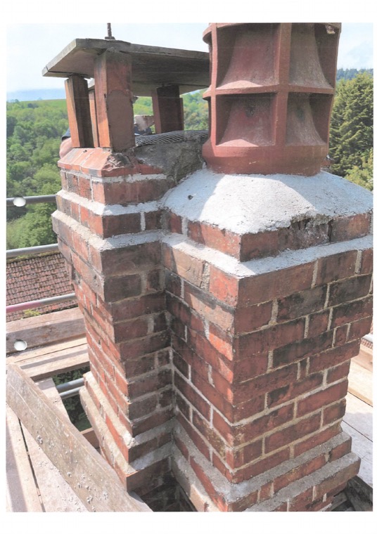 A brick chimney stack part-rebuilt, seen from the scaffold with fresh mortar and old pots alongside.