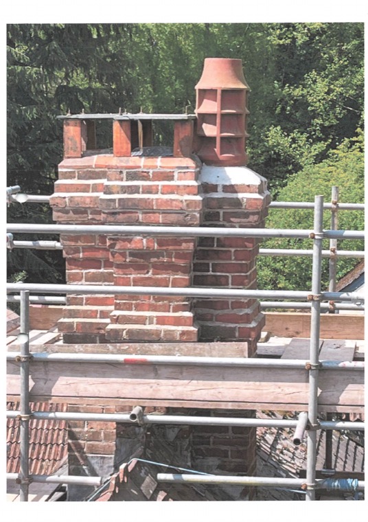 Two rebuilt brick stacks with tall chimney pots, framed by scaffolding against dark conifers.