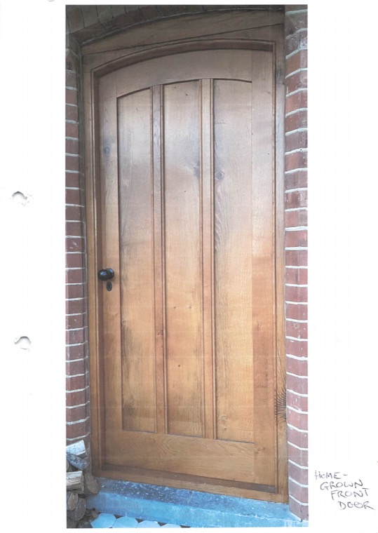 A new oak plank door with an arched head, set in a brick opening, annotated in pencil home-grown front door.