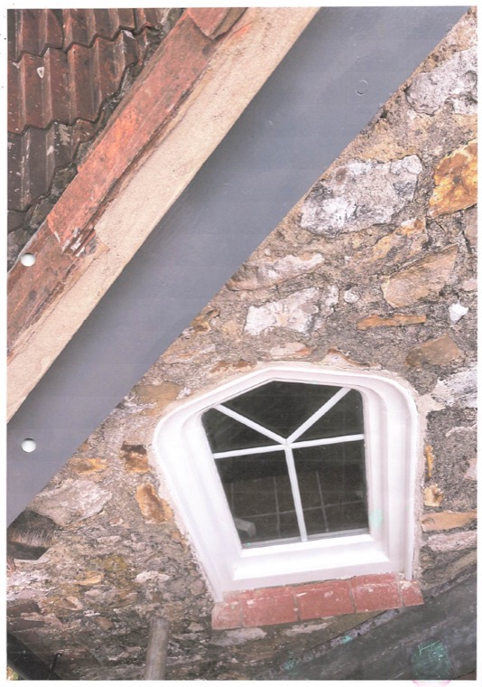 A small arched window in the rubble-stone gable, newly rendered around, beneath fresh leadwork.