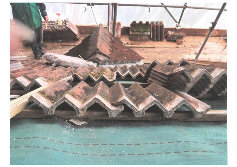 Reclaimed clay tiles stacked in rows on the scaffold platform, ready to be re-laid.