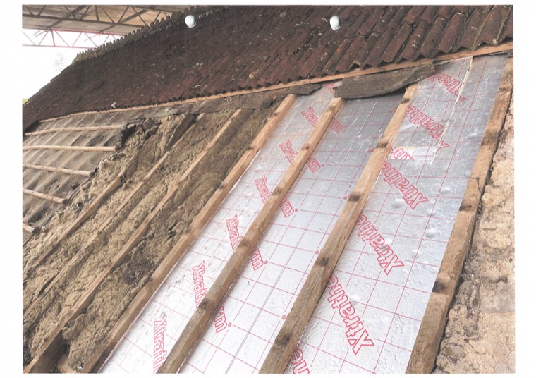 Foil-faced insulation boards fitted between and over the rafters, with the old tiling and loose fill visible alongside.
