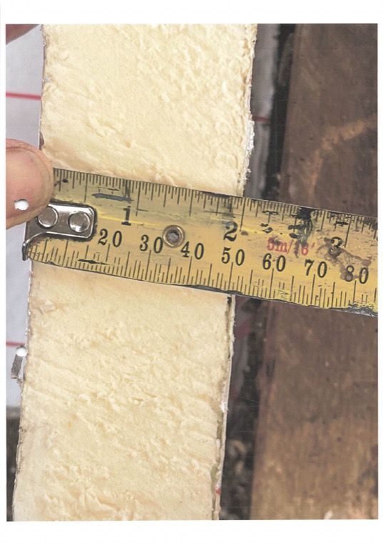 A tape measure held against the cut edge of an insulation board to show its thickness.